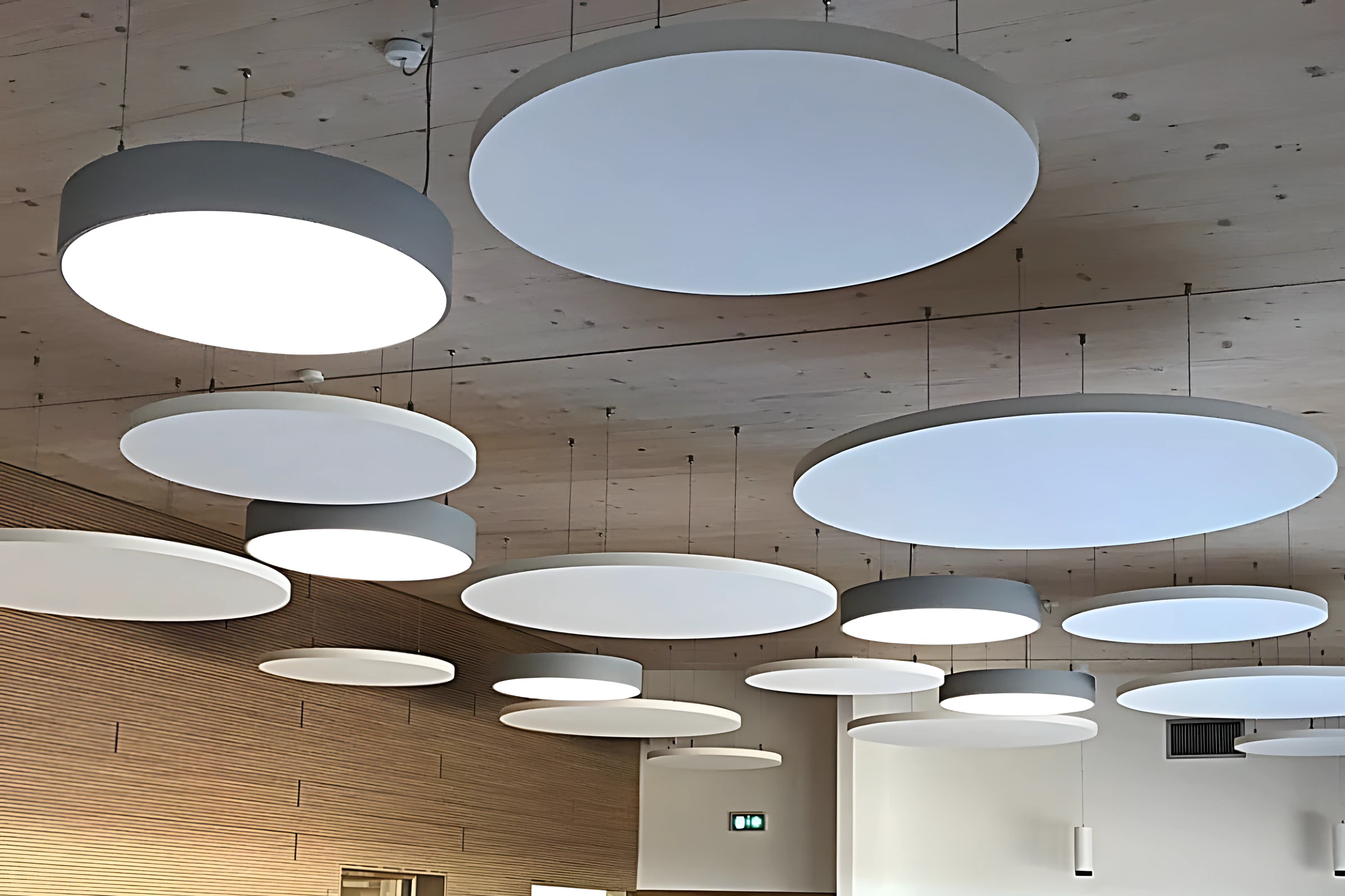 Îlots acoustiques ronds suspendus sous un plafond bois, dans une cafétéria